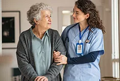 A caregiver walking a senior woman down a hallway
